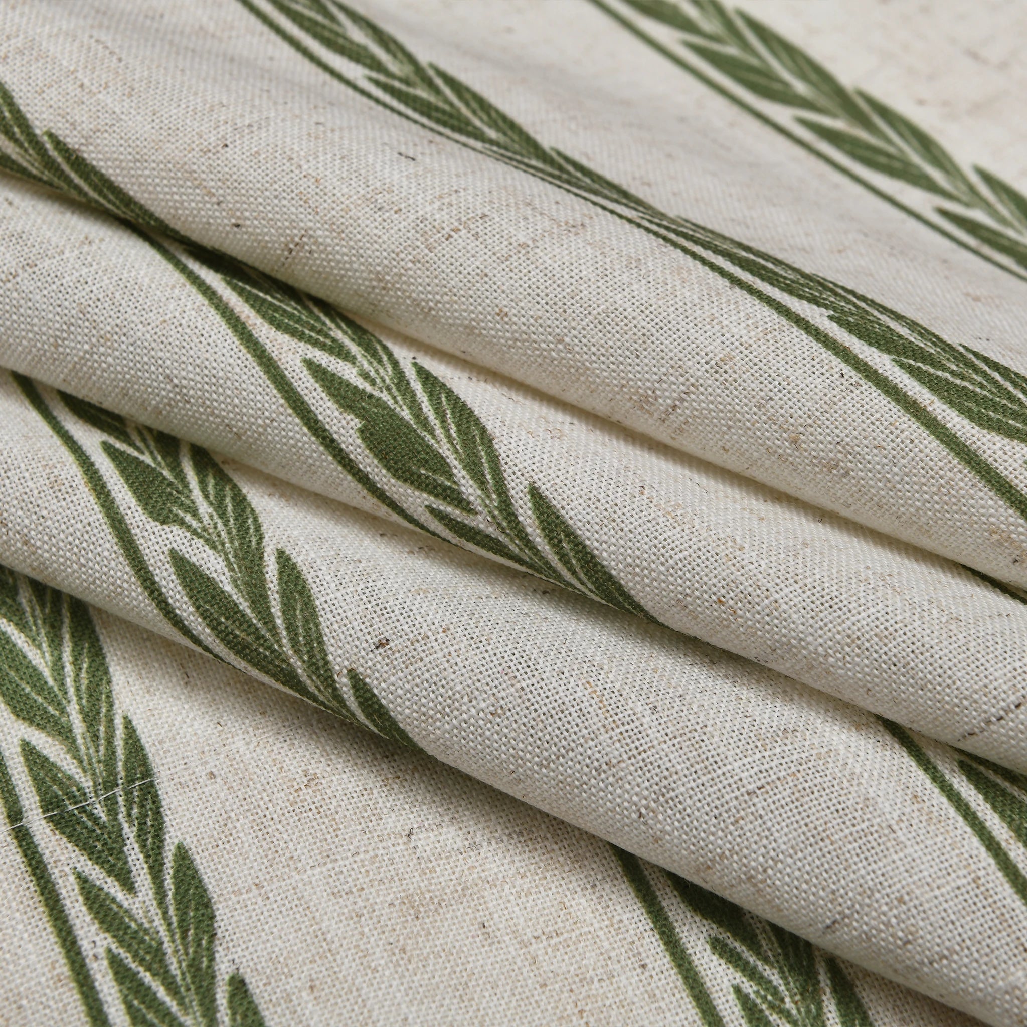 Green leaf patterned linen curtain fabric close-up, featuring natural beige texture and botanical design for elegant window decor.