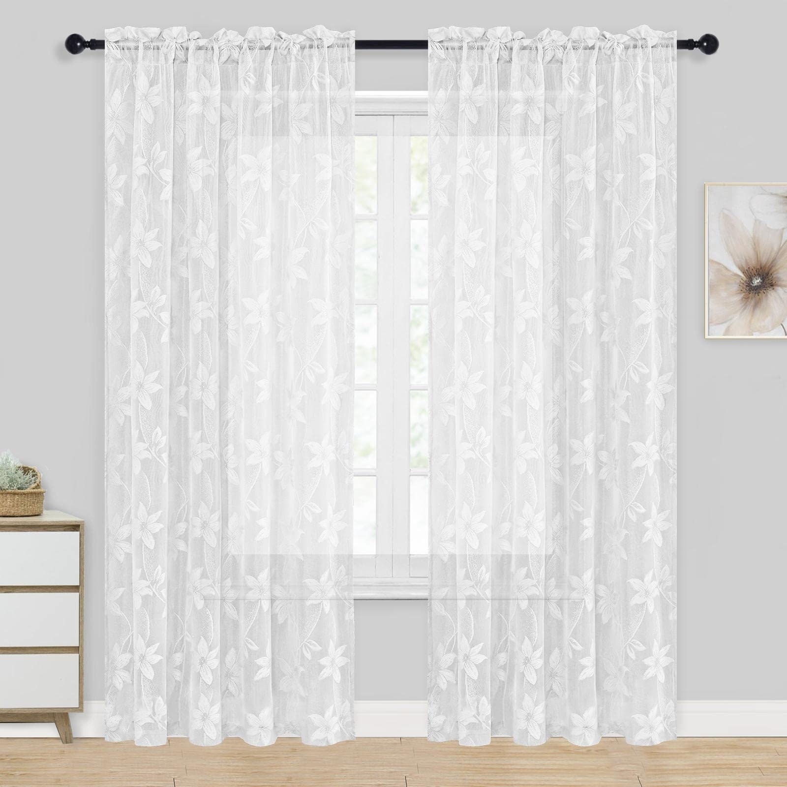 White floral lace curtains hanging in a room with a small table and decorative item.